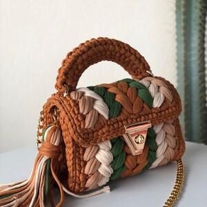 May include: A small brown, green, and white crocheted handbag with a gold chain strap and a tassel. The bag has a top handle and a gold clasp.