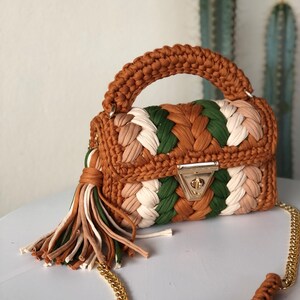 May include: A small, brown, green, and white crocheted handbag with a gold chain strap and a tassel. The bag has a woven design and a gold clasp.