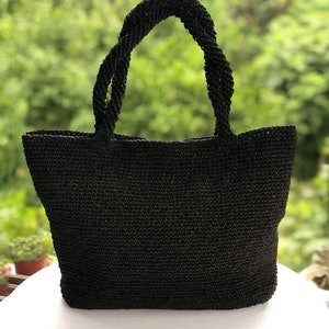 May include: A black tote bag constructed from a woven material with a textured surface. The bag features two sturdy, twisted handles attached to the top edge, providing a consistent dark aesthetic throughout the entire structure of the item.
