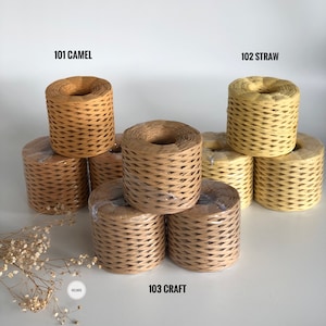 May include: Three spools of paper twine in different colors: camel, straw, and craft. The spools are stacked on a white surface.