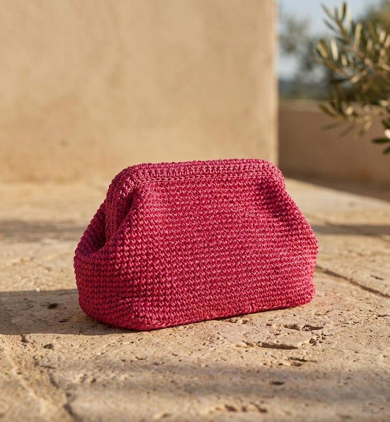 May include: A vibrant magenta clutch bag crafted with a dense, textured crochet stitch pattern. The accessory features a structured, rectangular frame with a kiss-lock closure mechanism, showcasing a consistent, uniform weave throughout the exterior.