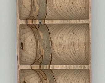 May include: A rectangular wooden tray with five carved compartments. The tray is made of light-coloured wood with darker, swirling grain patterns. The compartments are rounded and have a smooth finish.