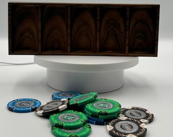 May include: A dark wood poker chip holder with five compartments sits above a collection of poker chips. The chips are blue, green, black, and white, with denominations of 10, 25, and 100.