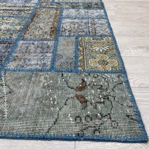 May include: A patchwork rug with a blue and beige color scheme. The rug is made of different pieces of fabric sewn together, creating a unique and interesting pattern. The rug has a frayed edge and is made of a soft, woven material.