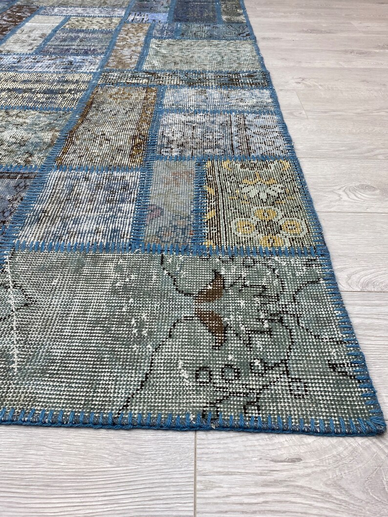 May include: A patchwork rug with a blue and beige color scheme. The rug is made of different pieces of fabric sewn together, creating a unique and interesting pattern. The rug has a frayed edge and is made of a soft, woven material.
