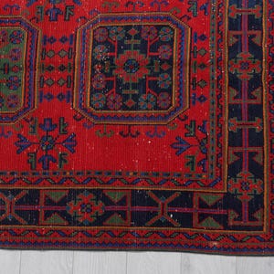 May include: A rectangular area rug featuring a vibrant red background with a repeating pattern of dark blue and green geometric shapes and floral motifs. The rug includes a wide dark blue border with intricate linear and symmetrical designs.