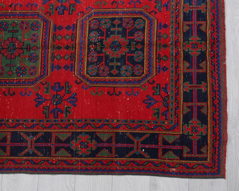 May include: A rectangular area rug featuring a vibrant red background with a repeating pattern of dark blue and green geometric shapes and floral motifs. The rug includes a wide dark blue border with intricate linear and symmetrical designs.