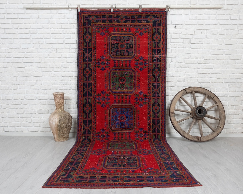 May include: A long rectangular rug featuring a vibrant red background with a dark blue border and four central geometric medallions in shades of blue, green, and red. The rug displays intricate repeating patterns throughout the field.
