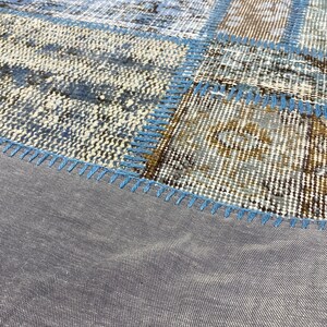 May include: A patchwork rug with a blue and brown color scheme. The rug is made of different pieces of fabric sewn together. The edges of the rug are finished with a blue stitching.