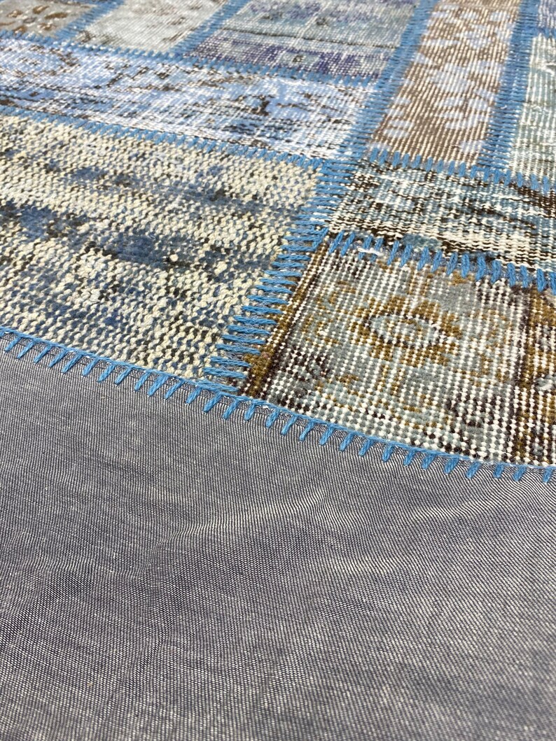 May include: A patchwork rug with a blue and brown color scheme. The rug is made of different pieces of fabric sewn together. The edges of the rug are finished with a blue stitching.