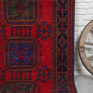 May include: A rectangular area rug featuring a vibrant red background with repeating geometric patterns in blue and green. The design includes central square motifs and a dark border with intricate linear details and floral-inspired accents.