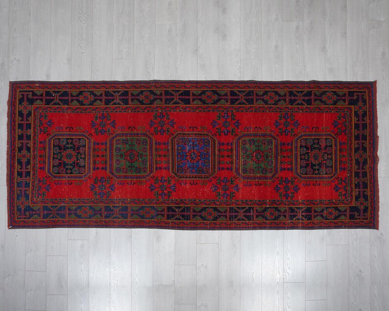 May include: A rectangular area rug featuring a vibrant red background with five prominent dark blue and green geometric medallions. The rug is framed by a wide, dark blue border decorated with repeating black and red linear patterns.