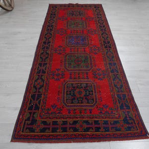 May include: A rectangular runner rug featuring a vibrant red field with five repeating geometric medallions in shades of blue and green. The border is dark blue with a repeating cross and diamond pattern, framed by thin red and blue lines.