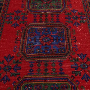 May include: A rectangular woven rug featuring a vibrant red background with repeating geometric patterns in blue and green. The design includes central octagonal motifs surrounded by stylized floral shapes and a dark blue border with geometric lines.