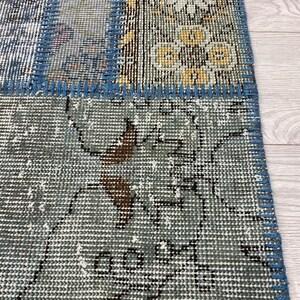 May include: A patchwork rug with a blue and gray color scheme. The rug is made of different pieces of fabric that have been sewn together. The rug has a fringe border.
