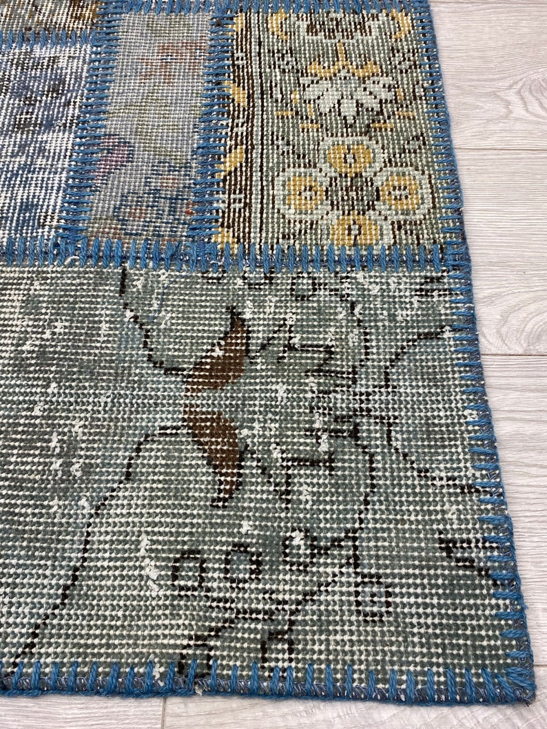 May include: A patchwork rug with a blue and gray color scheme. The rug is made of different pieces of fabric that have been sewn together. The rug has a fringe border.