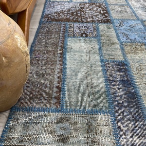 May include: A patchwork rug with a blue, brown, and white color scheme. The rug is made of different pieces of fabric that have been sewn together. The rug has a frayed edge and a textured surface.