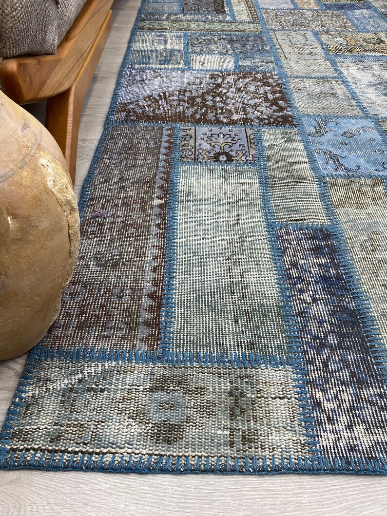 May include: A patchwork rug with a blue, brown, and white color scheme. The rug is made of different pieces of fabric that have been sewn together. The rug has a frayed edge and a textured surface.