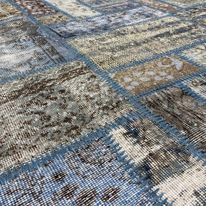 May include: A patchwork rug with a blue, brown, and white color scheme. The rug is made of different pieces of fabric that have been sewn together. The rug has a distressed look, with some of the fabric pieces being frayed and worn.