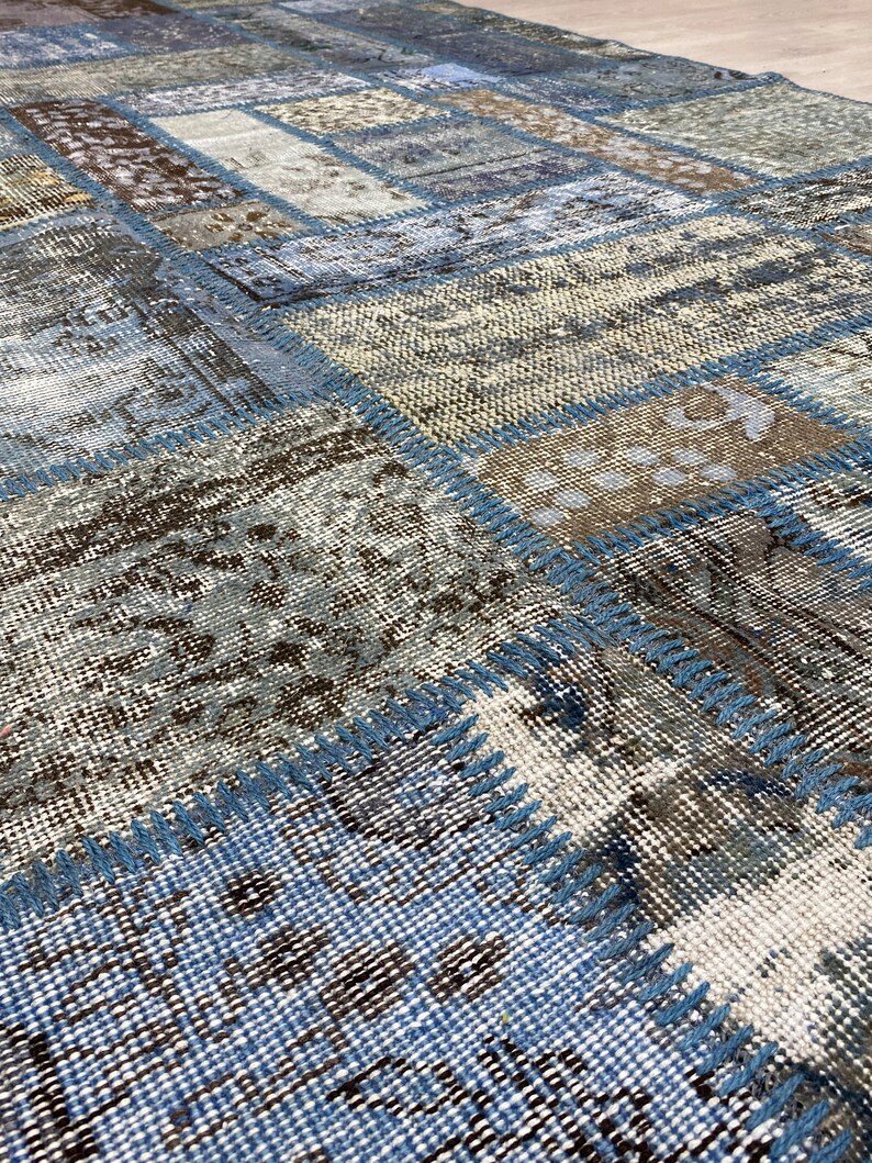 May include: A patchwork rug with a blue, brown, and white color scheme. The rug is made of different pieces of fabric that have been sewn together. The rug has a distressed look, with some of the fabric pieces being frayed and worn.