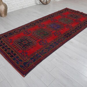 May include: A rectangular area rug featuring a vibrant red background with a series of repeating dark blue and green geometric medallions. The border consists of intricate dark blue patterns that frame the central design of the woven textile.