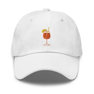 Pode incluir: Bon&eacute; de beisebol branco com um coquetel laranja bordado com uma fatia de lim&atilde;o e um canudo.