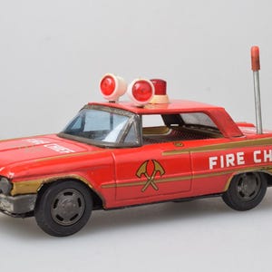 Peut inclure: Une voiture jouet en métal rouge vintage avec l'inscription FIRE CHIEF sur le capot et les côtés. Elle comporte deux lumières circulaires rouges sur le toit, une petite sirène rouge, une antenne argentée et des détails dorés. Roues noires.