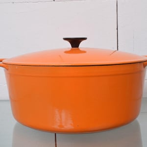 Op de afbeelding: Een feloranje geëmailleerde gietijzeren braadpan met een bijpassend deksel en een donkerbruine knopgreep. De pan is voorzien van twee zijhandgrepen en een gladde, glanzende afwerking, met een brede, ronde vorm voor koken en voedselbereiding.