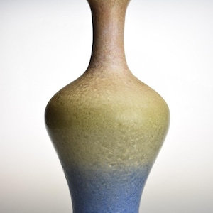 Könnte beinhalten: Eine Keramikvase mit ausgestelltem Rand und verjüngtem Hals, der in einen abgerundeten Körper übergeht. Die Oberfläche weist ein strukturiertes, gesprenkeltes Finish mit einem Farbverlauf von warmem Hellbraun oben bis Olivgrün und Blau an der Basis auf.