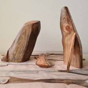 May include: Three wooden sculptures made from a single piece of wood with a natural wood finish. The sculptures are arranged on a wooden surface with a natural wood grain.