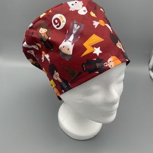 Könnte beinhalten: Eine weinrote OP-Haube mit einem sich wiederholenden Muster aus Zeichentrickfiguren, Blitzen und anderen thematischen Grafiken. Die Haube ist so konzipiert, dass sie bequem sitzt und aus einem weichen, flexiblen Material besteht.