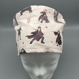 Könnte beinhalten: Eine cremefarbene OP-Haube mit einem Muster von Harry Potter-Charakteren. Die Haube zeigt Illustrationen von Harry, Ron, Dobby und anderen, mit roten Sternen. Ein thematisches Accessoire.