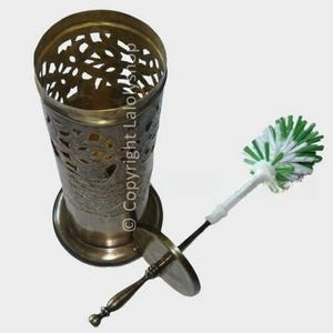 Può includere: Un porta spazzolino per WC in ottone con un intricato design floreale e uno spazzolino per WC bianco e verde con un manico in legno.