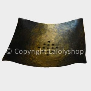 Può includere: Un piatto in ceramica nero e oro con un bordo ondulato e una griglia di piccoli fori al centro.