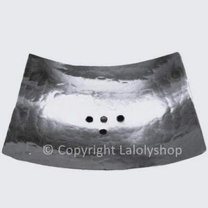 Può includere: Un portasapone in argento con una forma curva e tre fori di scarico. Il portasapone ha una texture martellata e una superficie liscia e riflettente. © Copyright Lalolyshop