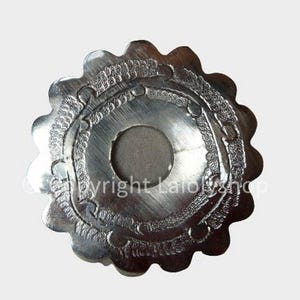 Può includere: Un pezzo decorativo in metallo argentato con un bordo a festoni e disegni incisi intricati. Il pezzo ha un foro circolare al centro.