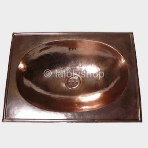 Pode incluir: Uma pia de banheiro ovalada na cor cobre com uma moldura retangular. A pia possui um ralo e três orifícios para a torneira. A superfície reflete a luz, criando uma aparência texturizada. O texto "© lalolyshop" é visível.