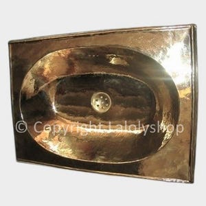 Può includere: Un lavabo ovale in ottone martellato con un foro di scarico. Il lavabo è montato a parete e ha un aspetto rustico e antico.