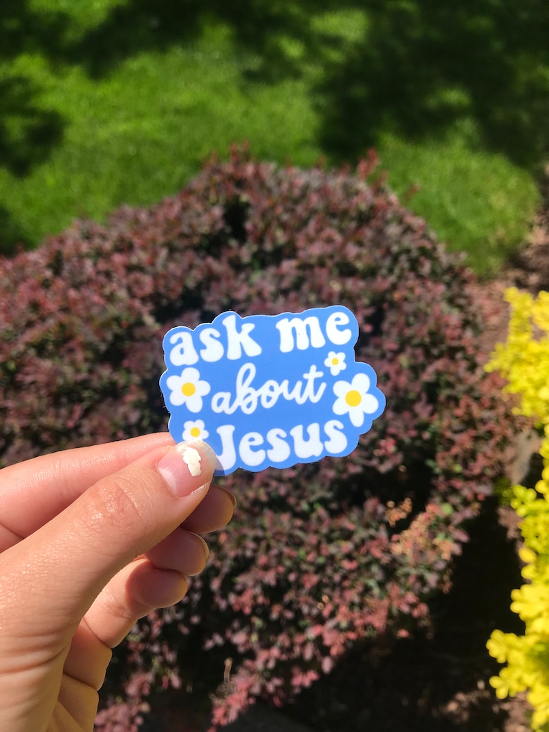 May include: A blue sticker with white daisies and the text "ask me about Jesus" in white.