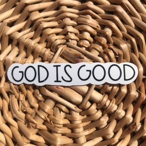 Puede incluir: Pegatina blanca con texto negro que dice "GOD IS GOOD" sobre un fondo de mimbre tejido.