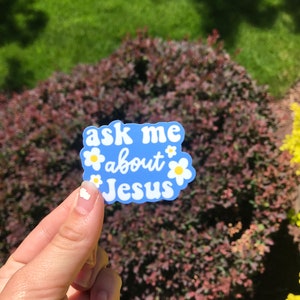 May include: A blue sticker with white text and yellow flowers that says "ask me about Jesus".