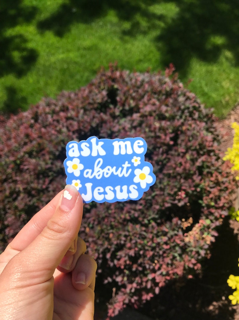 May include: A blue sticker with white text and yellow flowers that says "ask me about Jesus".