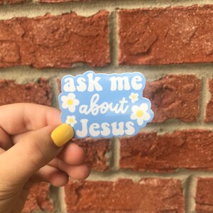 May include: A blue sticker with white daisies and the text "ask me about Jesus" in a white, cursive font.