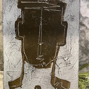 Op de afbeelding: Abstract kunstwerk op een getextureerd rechthoekig oppervlak. De achtergrond is wit en grijs. Een bruin, gestileerd gezicht is op het oppervlak geschilderd met witte contouren. Onderaan het kunstwerk bevindt zich een kleine cirkel.