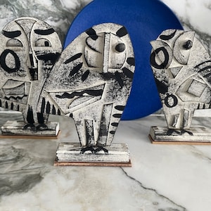 Può includere: Tre sculture di gufo in ceramica bianca e nera su basi in legno. I gufi sono stilizzati e astratti, con forme e motivi geometrici.