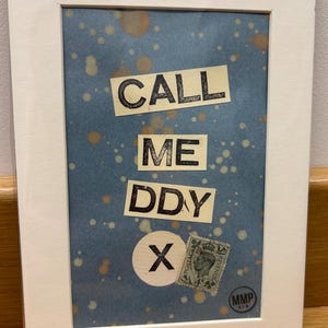 May include: Framed artwork with the text "CALL ME DDY X" in a collage style. The background is blue with brown and yellow splatters. A vintage postage stamp and a white circle with an "X" are also included.