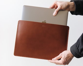 May include: A brown leather laptop sleeve with the word "MUSE" embossed on the front. A silver laptop is partially inside the sleeve.