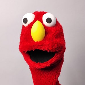 May include: Red felt hand puppet with a yellow beak, black mouth, and white eyes. The puppet is on a black stand.