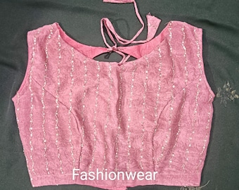 May include: A sleeveless pink blouse featuring a textured fabric with vertical silver sequin stripes and a tie-back closure at the neckline. The garment displays the word Fashionwear printed in white at the bottom centre of the front panel.