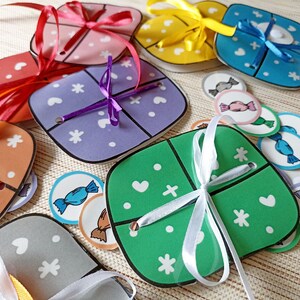 Puede incluir: Un conjunto de cajas de regalo de cartón cuadradas y coloridas con acentos de cinta y lazo. Cada caja tiene un patrón y un color diferente, incluyendo morado, verde, naranja, amarillo y azul. Las cajas están rodeadas de pequeñas fichas redondas y coloridas con forma de caramelo.